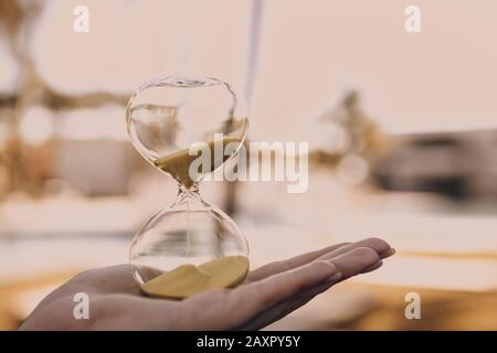 Hourglass in a female hand on a blurry light background, a symbol of the passage of time and the implementation of important life matters Stock Photo