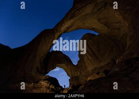 Silhouette of hiker framed by Double arch under starry sky in Arches Stock Photo