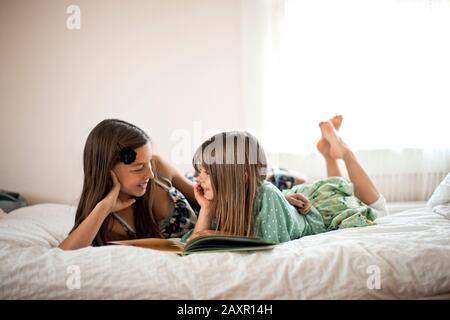 Preteen lies on a bed talking to her elementary age sister. Stock Photo