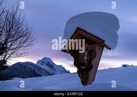 Path cross above Mittenwald in the Bavarian Alps, in the background the Wetterstein with colored cloud train after sunset in winter Stock Photo