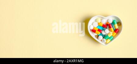 Heart shaped plate with colorful medical pills in capsule on yellow background. Top view with copy space. Healthcare, pharmacy, medicine concept. Medi Stock Photo