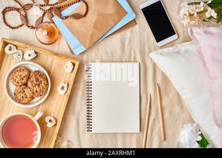 Mockup with notepad on bed and women's accessories, tea, cookies, pillows, flowers, letter, notebook. Cozy women's creative world. . Stock Photo