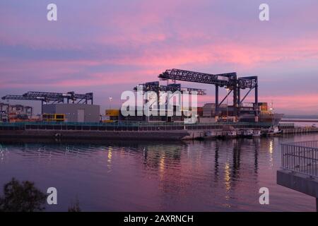 A beautiful pink and blue sunset over Hutchison Ports Sydney, Port Botany Container Terminal gantry and cargo ship reflected in the water Stock Photo