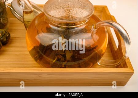 Flower tea brewed in a glass teapot on a wooden tray on a white background. Close up Stock Photo
