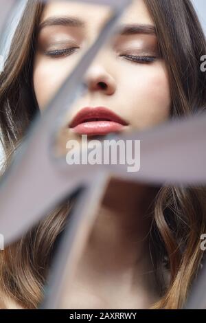 Young woman looks in a broken mirror. Portrait of beautiful female in the mirror shards. Eyes closed. Stock Photo
