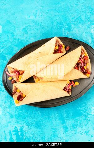 Burritos, sandwich wraps, top-down shot on a vibrant blue background. Mexican tortillas stuffed with ground meat, rice, beans, onions, and chilis Stock Photo