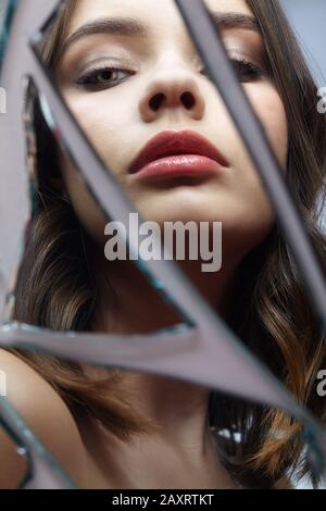 Young woman looks in a broken mirror. Portrait of beautiful female in the mirror shards. Stock Photo