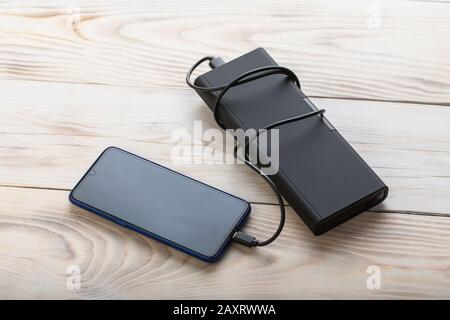Smartphone charging with black power bank on wood table background. Stock Photo