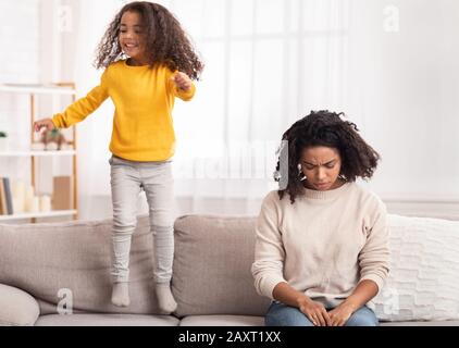 Exhausted Mother Sleeping While Hyperactive Daughter Jumping On Sofa Indoor Stock Photo