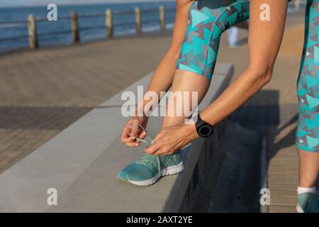 Female jogger tying her shoe laces on seaside Stock Photo