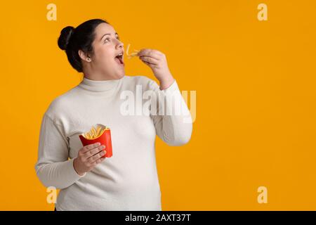 Overweight Girl Eating French Fries With Great Appetite Over Yellow Background Stock Photo