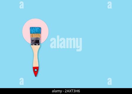 Renovation picture. Blue background with one paint brush located on pink circle. Flat lay, top view, copy space. Stock Photo