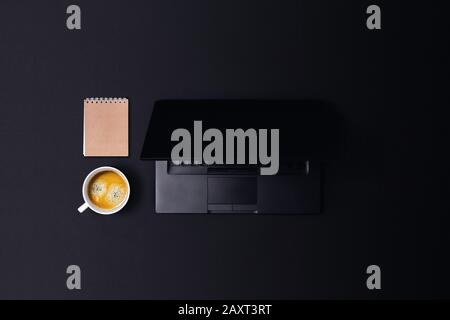 Modern workspace in dark color with laptop, coffee and notepad. Central composition. Stock Photo