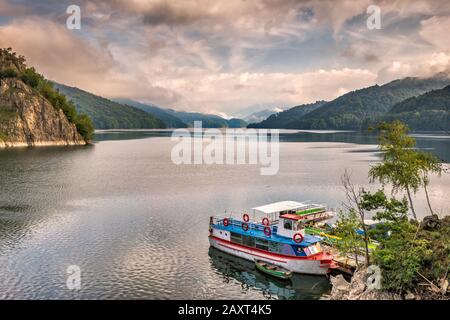 Boats at Lake Vidraru, view from Transfagarasan Road, Fagaras Mountains shrouded in low clouds in early morning, Southern Carpathians, Romania Stock Photo