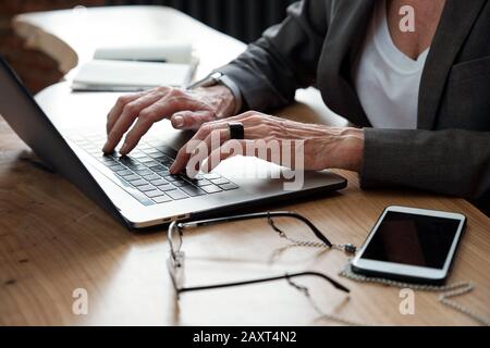 Close-up of unrecognizable businesswoman with ring sitting at table with smartphone and glasses and working on online project Stock Photo