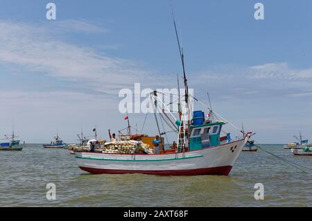 Fishermen working on the deck of an anchored Peruvian Inshore Fishing Boat waving as a Vessel passes. Stock Photo
