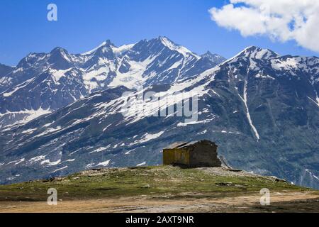 An abandoned hut on top of a mountain with a view of snowy mountains at Rohtang Pass, Kullu, Himachal Pradesh. Stock Photo