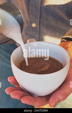 Man holding cup of coffee and pouring milk in espresso Stock Photo
