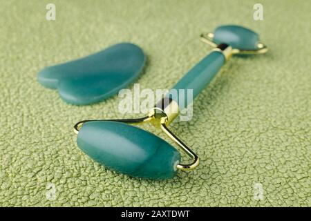 real jade facial roller and massage stone gua sha on green background, closeup Stock Photo