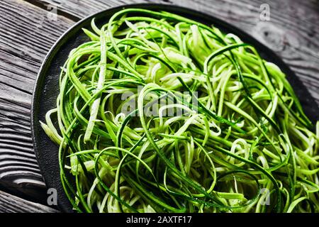 close-up of fresh zucchini noodles, zoodles on a black plate on a rustic wooden table, horizontal view from above Stock Photo