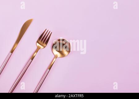 Elegant golden cutlery on pink background Stock Photo