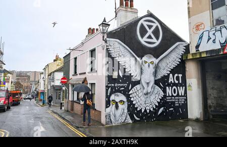 Brighton UK 13th February 2020 - Umbrellas are out in central Brighton by an Extinction Rebellion mural on a wet and windy day as Storm Dennis approaches Britain with high winds and flooding expected to cause more damage this coming weekend: Credit Simon Dack / Alamy Live News Stock Photo