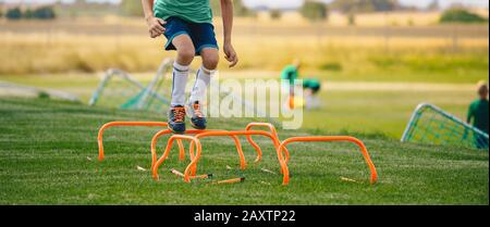 Low section portrait of unrecognisable boy jumping over hurdles in football field. Kid young athletes training with football equipment. Soccer speed d Stock Photo
