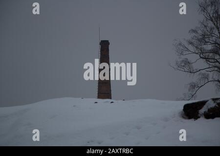 Pipes of a plant on a background of gray sky. Brick pipes peep out from behind a hillock. Industrial area. Cloudy weather in winter. Air emissions fro Stock Photo