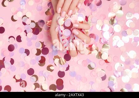 Beautiful female hands with colorful round paper confetti poured on pink background. Flat lay. Holiday concept. Copy space. Mockup for your design. Stock Photo