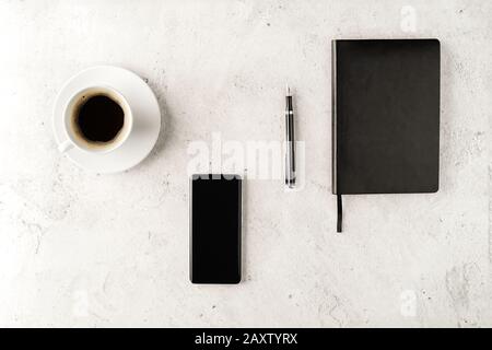 Up-to-date smartphone with notebook, fountain pen and cup of coffee on concrete background. Workstation concept flat lay. Coffee break top view. Mocku Stock Photo