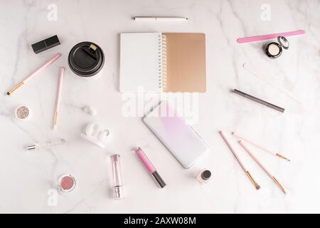 Feminine workspace in flat lay style with opend notepad, up-to-date smartphone mockup, coffee paper cup, cosmetics and manicure products on marble bac Stock Photo