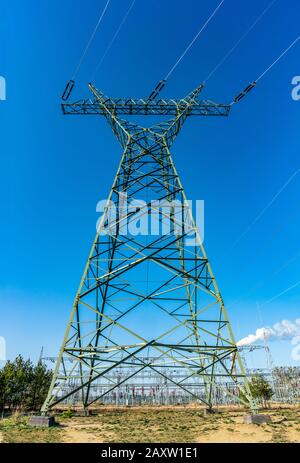 Green metal electrical tower on a field with a transformer station in the background Stock Photo