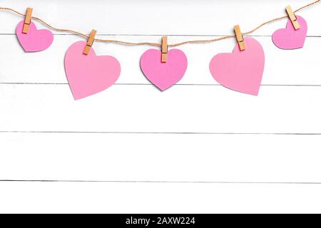 Clothespins with colored hearts hanging on rope behind white wooden surface. Copy space, top view. Stock Photo