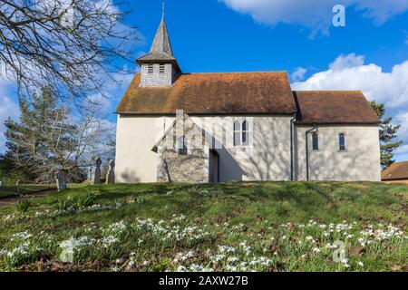 Exterior of historic Norman Wisley Church, Parish of Wisley with Pyrford, Surrey, with snowdrops in flower in the churchyard on a sunny winter day Stock Photo