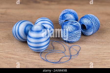 Blue striped Easter eggs and cotton yarn in decorative skeins on wooden background. Group of streaked decorated egg shells and hanks of sewing thread. Stock Photo