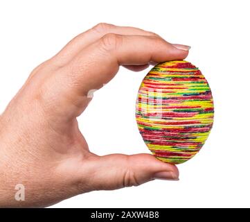 Female hand holding multicolored golden Easter egg shell. Traditional chicken eggshell decorated by glued thin twine painted by various bright colors. Stock Photo