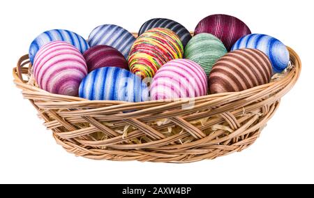 Colorful stripy ornate Easter eggs in wicker basket. Close-up of handmade holiday decorations wrapped in thin cotton yarn glued to chicken egg shells. Stock Photo