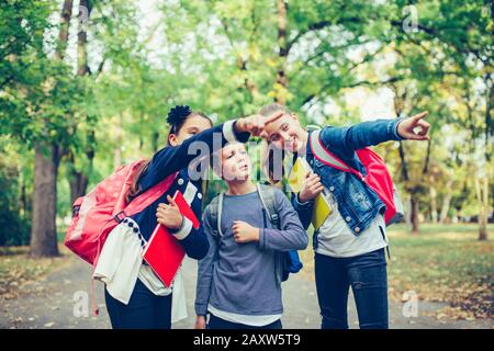 Back to school. Close up three happy friends with backpacks laughing and having fun in the park. Boy and girl holding books on the first school day. K Stock Photo