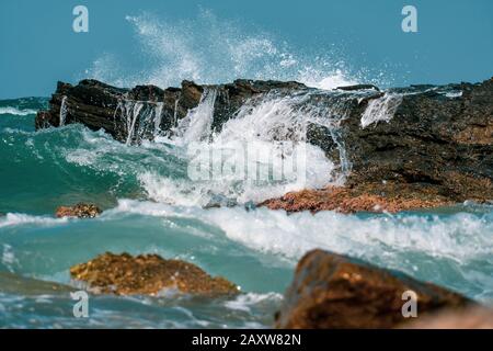 Waves crashing on rocks close-up under the bright sun