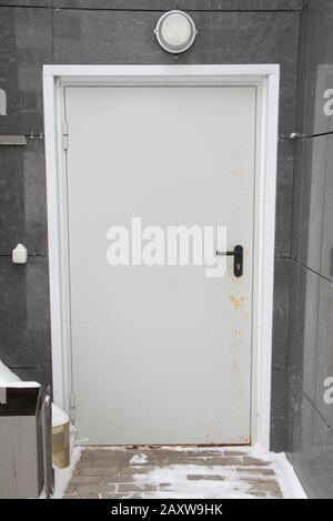 White front door in gray paneled wall and snow covered tile road. Stovk photo with empty space for text. Stock Photo