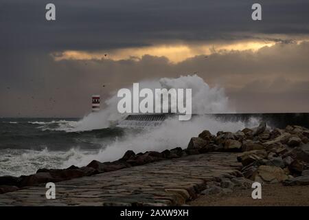 Dramatic stormy winter sunset at the Douro river mouth with big wave splash against north pier and beacon. Stock Photo