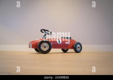 Vintage red toy racing car seen from side, against grey wall and on wooden floor Stock Photo
