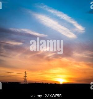Sunset and electricity pylon. A dramatic sky and sunset scene in rural England with the silhouette of a UK National Grid electricity pylon. Stock Photo