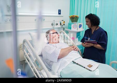 Doctor with digital tablet making rounds, talking with senior couple in hospital room Stock Photo
