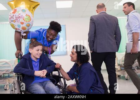 Doctor and nurse talking with boy patient in wheelchair in hospital ward Stock Photo