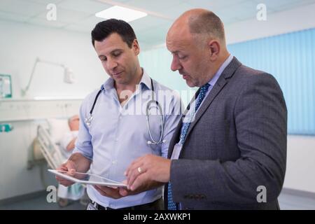 Male doctors with digital tablet making rounds, consulting in hospital room Stock Photo