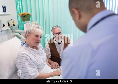 Doctor making rounds, talking with senior couple in hospital room Stock Photo