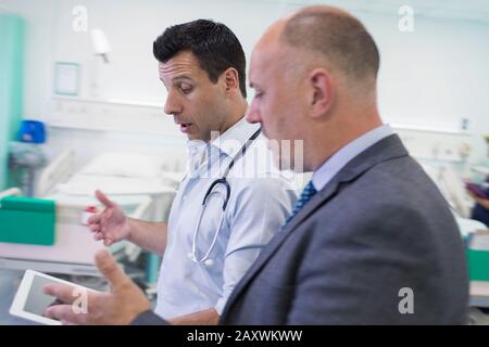 Male doctors with digital tablet making rounds, consulting in hospital room Stock Photo