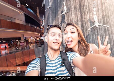 26 November 2019, UAE, Dubai: Happy Couple taking selfie photo at the famous waterfall with jumping men in Dubai Mall. Tourist destination Stock Photo
