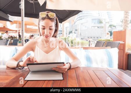 Asian woman browsing menu in electronic tablet. Choosing dish in outdoor cafe Stock Photo